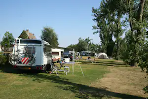 Wohnmobil auf dem Stellplatz mit Fahrrad am Heck, Markise und Campingstühlen, weitere Fahrzeuge und Zelte im Hintergrund.