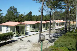 Reihen von Bungalows mit Terrassen auf einem Kiesweg, umgeben von Bäumen und Rasenfläche.