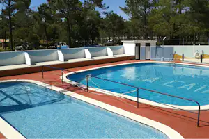 Camping-Pool mit blauem Wasser, Liegen auf der Terrasse und Bäumen im Hintergrund.