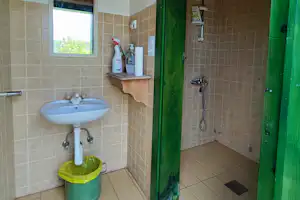 Camping-Badezimmer mit Waschbecken, grüner Tür, Dusche und Fliesenboden, Holzdecke und Handtuchhalter an der Wand.