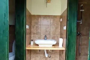 Camping-Badezimmer mit Waschbecken auf Holzplatte, Fliesenboden und grünen Türen, im Hintergrund Toilette und Dusche.