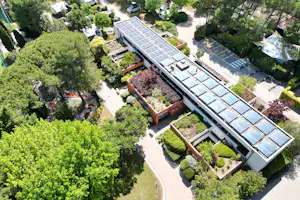 Luftaufnahme eines Campingplatzes mit Solardach-Reihen, Wegen und Stellplätzen zwischen Bäumen und gepflegten Grünflächen.