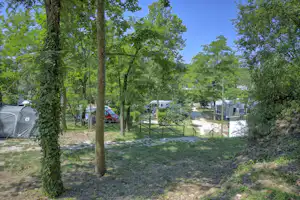 Campingstellplätze im Grünen mit Zelten, Wohnwagen und einem Weg zwischen Bäumen und Hecken.