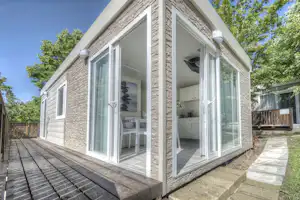 Modernes Ferienhaus mit Steinfassade, großen Glas-Schiebetüren und Holzterrasse, Blick auf Küchenzeile im Inneren.