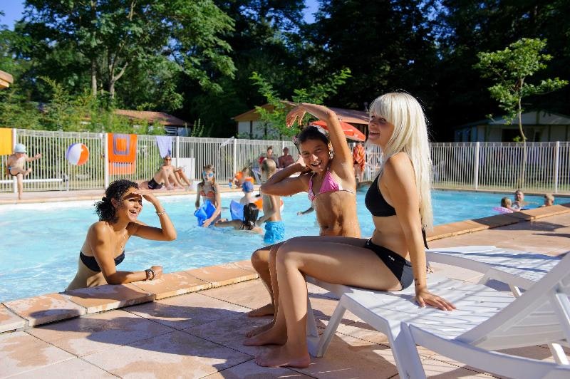 Frau und Kind liegen auf Sonnenliegen am Camping-Pool, im Hintergrund planschen weitere Kinder im Wasser.