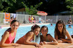 Kinder am Poolrand im Camping, im Hintergrund weitere Gäste und ein Sonnenschirm neben dem Becken.