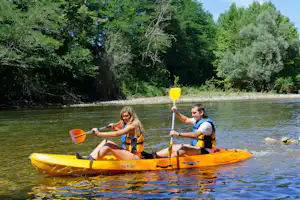 Zwei Personen paddeln im orangefarbenen Kanu auf einem Fluss, umgeben von dichtem Grün und Bäumen am Ufer.
