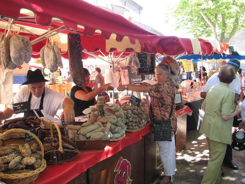 Fischstand unter rotem Zelt auf einem Campingmarkt, mit Körben voller Fische und mehreren Personen am Tisch.
