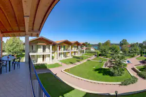 Blick auf die Ferienanlage: überdachte Terrasse, Gartenwege, Rasen und Reihen von grünen und weißen Apartments.