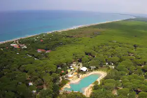 Luftaufnahme eines Campingplatzes mit kleinem Strand, türkisfarbenem Wasser und vielen Bäumen an einer Küstenbucht.