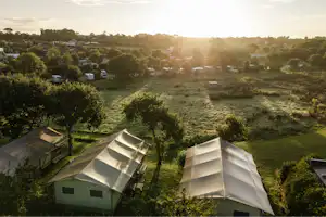 Zwei Campingzelte auf einem gepflegten Rasen, umgeben von Bäumen, mit Blick auf weitere Stellplätze im Hintergrund.