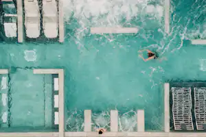 Schwimmbecken mit türkisfarbenem Wasser, Leiter und Sprungbereich; im Hintergrund ein Poolrand und ein weiteres Beckenbecken.