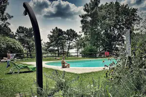 Campingpool mit Liegestuhl und Sonnenschirm, im Hintergrund Bäume und ein Kind am Beckenrand auf dem Campingplatz.
