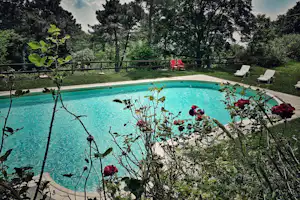 Schwimmbecken im Campinggarten mit Liegestühlen, rotem Stuhlset und Blick auf Bäume und Hecken.