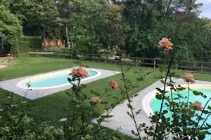Zwei kleine Camping-Pools im Garten mit Rasen, Holzgeländer und Bäumen im Hintergrund.
