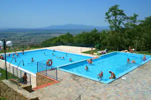 Großes Camping-Schwimmbecken mit mehreren Bereichen, Liegen und Blick auf Berge und grünes Umland.