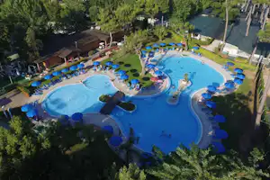 Luftaufnahme von zwei großen Schwimmbecken mit blauen Liegen am Campingplatz, umgeben von Bäumen und Wegen.