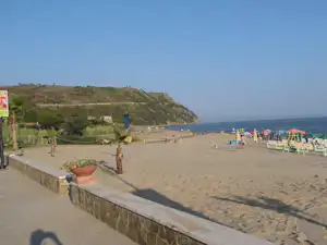 Sandstrand am Campingplatz mit Liegen, Sonnenschirmen, Spielbereich und Blick auf die Küste zwischen Hügeln.
