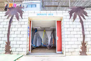 Eingang zu einem Segel-Depot mit aufgestellten Segeln im Innenraum, Ziegelmauer und roter Tür am Campingplatz.