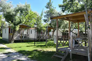 Holzterrassen und Mobilheime auf dem Campingplatz, umgeben von Bäumen und Rasenfläche.