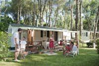 Camping Villaggio Baia Domizia  -  Mobilheim mit Terrasse zwischen Bäumen auf dem Campingplatz