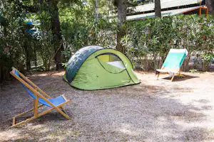 Grünes Zelt auf einem Campingplatz mit zwei Liegestühlen, Kiesboden und Bäumen im Hintergrund.