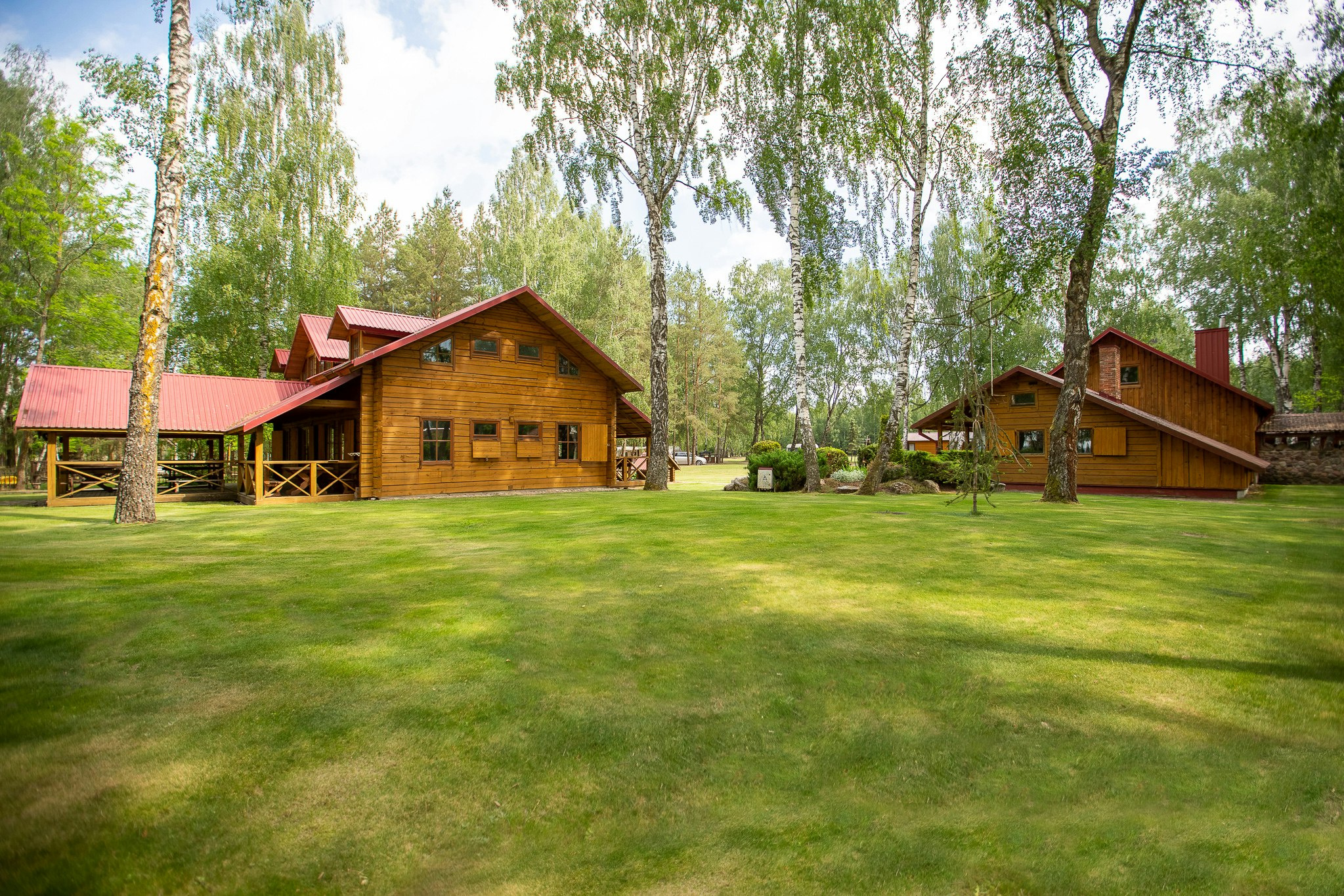 Holzhäuser und Bungalows auf einem Campingplatz, umgeben von Rasen und hohen Bäumen, mit Wegen zwischen den Unterkünften.