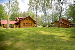 Holzhäuser und Bungalows auf einem Campingplatz, umgeben von Rasen und hohen Bäumen, mit Wegen zwischen den Unterkünften.
