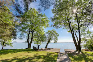 Uferpromenade am See mit Holzsteg, Rasenfläche und Bäumen im Vordergrund, Blick über das Wasser.
