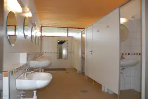 Gemeinschaftsbad im Camping: mehrere Waschbecken, Spiegel und Türen, geflieste Wände und Boden.