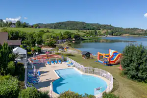 Campingplatz mit beheiztem Pool, Sonnenliegen und Rutsche, Blick auf den Fluss und grüne Hügel im Hintergrund.