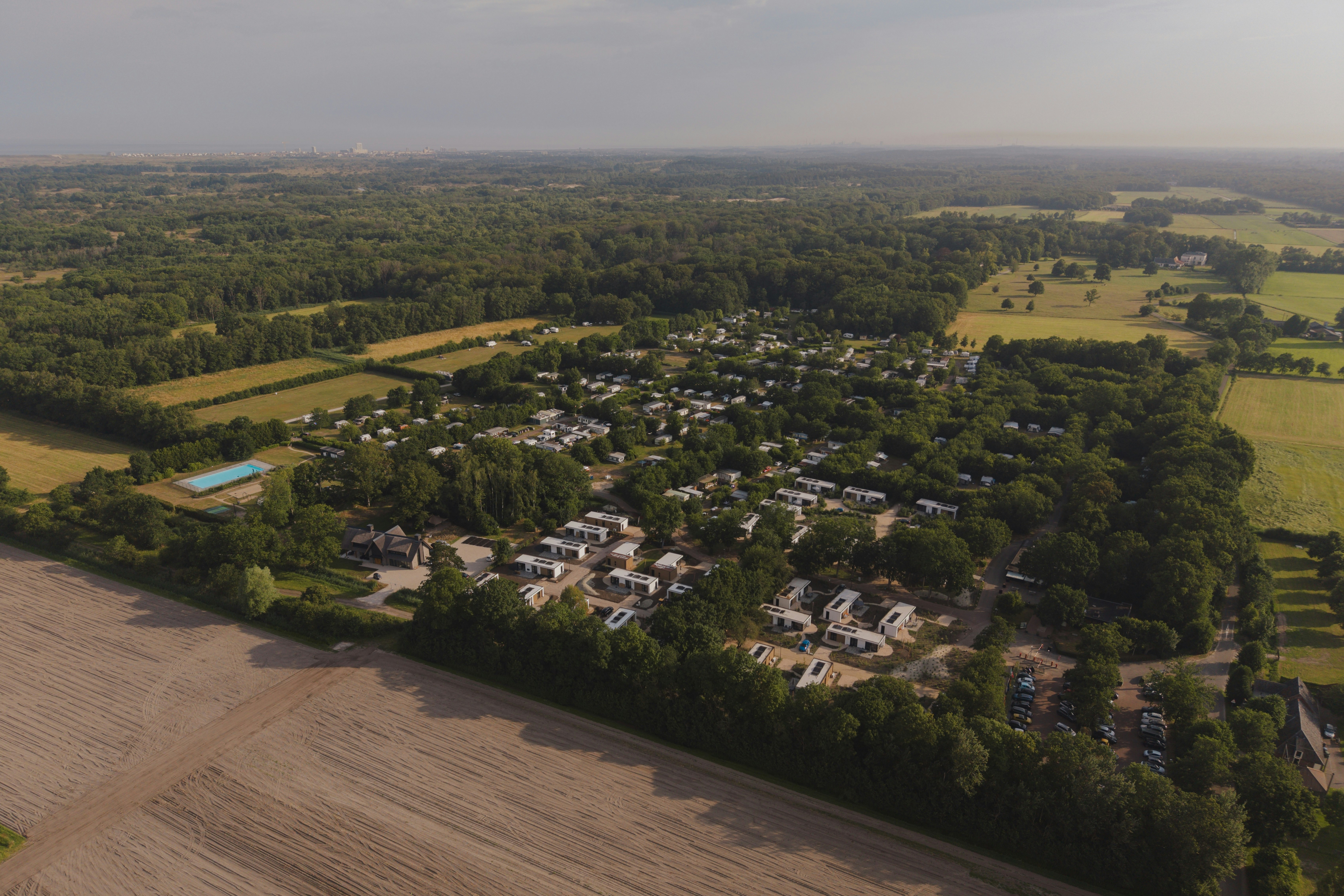 Luftaufnahme eines Campingplatzes mit mehreren Wohnmobilen und Zelten, umgeben von Feldern, Wäldern und Wegen.