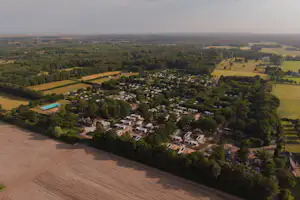 Luftaufnahme eines Campingplatzes mit mehreren Wohnmobilen und Zelten, umgeben von Feldern, Wäldern und Wegen.