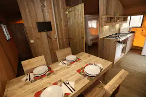 Holzhütte mit Esstisch, weißen Tellern und Küchenzeile mit Herd und Spüle im Innenraum.