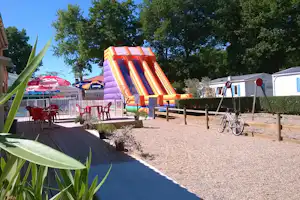 Aufblasbares Hüpfburg-Spielgerät auf dem Campingplatz, mit Terrasse, Tischen, Stühlen und Fahrrad neben dem Zaun.