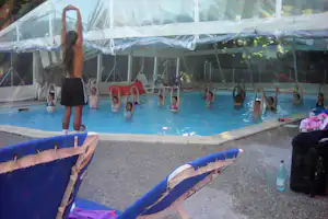 Campingpool unter einer großen Zeltplane, im Hintergrund Liegen und Kinder im Wasser.