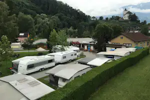 Campingplatz mit Wohnwagen und Vorzelten, gepflegten Wegen und Bäumen; im Hintergrund ein Schloss auf dem Hügel.
