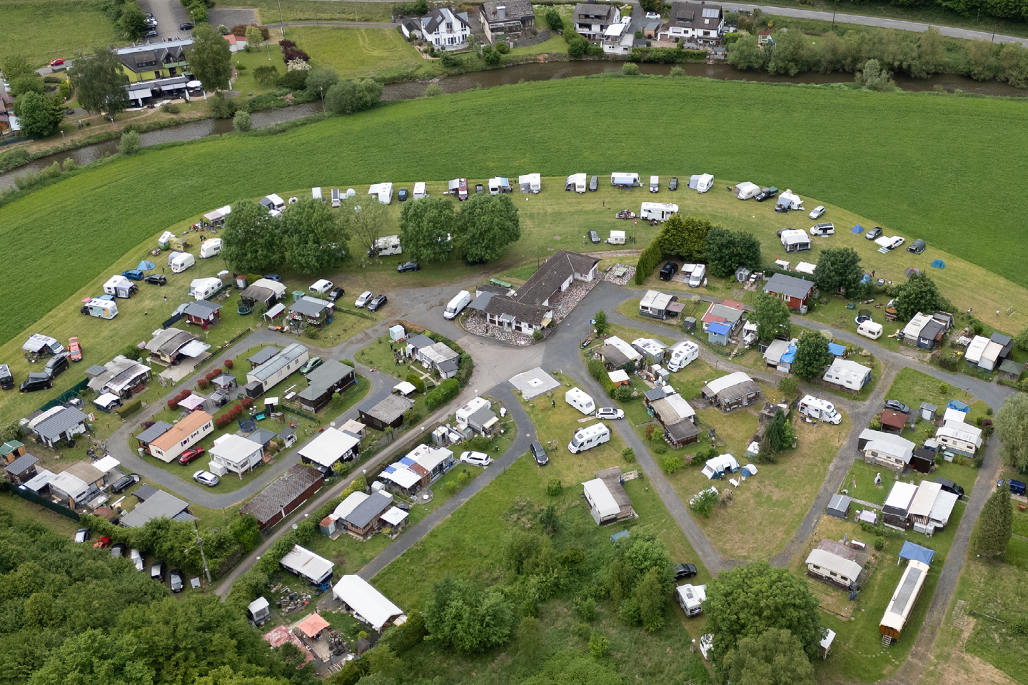 Luftaufnahme eines Campingplatzes mit vielen Wohnwagen und Zelten, Wegen zwischen Stellplätzen und grünen Wiesen rundherum.