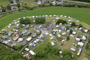 Luftaufnahme eines Campingplatzes mit vielen Wohnwagen und Zelten, Wegen zwischen Stellplätzen und grünen Wiesen rundherum.