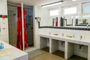 Camping-Badezimmer mit Waschbecken, Spiegeln und roten Duschvorhängen in hell gefliesten Wänden.