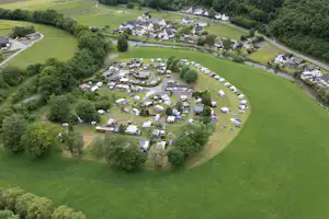 Luftaufnahme eines Campingplatzes mit vielen Stellplätzen, Wohnwagen und Zelten inmitten von grünen Wiesen und Bäumen.