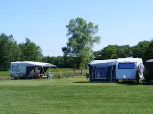 Zwei Wohnwagen mit Vorzelten auf grünem Campingplatz, dazwischen Rasen und kleine Sitzgarnituren, im Hintergrund Bäume.