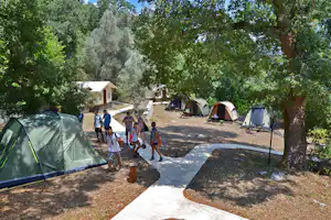Zeltreihe auf einem Campingplatz mit Kieswegen, Bäumen und mehreren Zelten im Hintergrund.