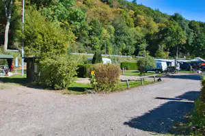 Campingplatz mit Zeltbereich, Wohnwagen und Fahrrädern am Rand, umgeben von Bäumen und grünen Hügeln.