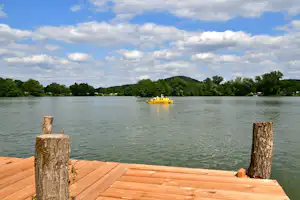 Blick vom Holzsteg auf den See mit zwei Personen im gelben Kanu und Bäumen am Ufer.