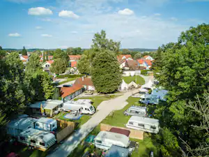 Campingplatz mit Wohnwagen und Zelten, gepflasterter Weg, Rasenflächen und viel Grün zwischen Häusern im Hintergrund.