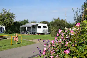 Wohnmobil mit Vorzelt auf einem Campingplatz, umgeben von Hecken, Rasen und Blumen im Vordergrund.