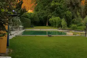 Schwimmbecken auf einer Campinganlage mit Rasen, Steinmauer und Bäumen im Hintergrund.