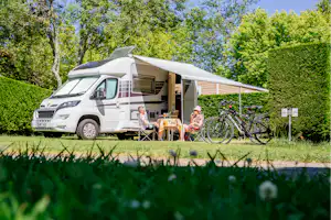 Wohnmobil auf dem Campingplatz mit Markise, Tisch und Stühlen sowie Fahrrädern neben dem Fahrzeug.
