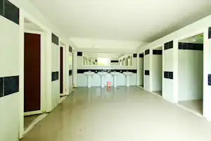 Waschraum im Campinghaus mit mehreren weißen Waschbecken, Fliesenboden und langen Reihen von Türen und Wänden.